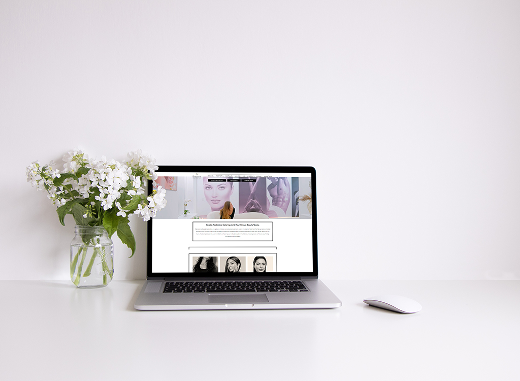Laptop displaying a beauty and aesthetics website on a clean, minimalist desk with a vase of white flowers, emphasizing a modern and stylish workspace.