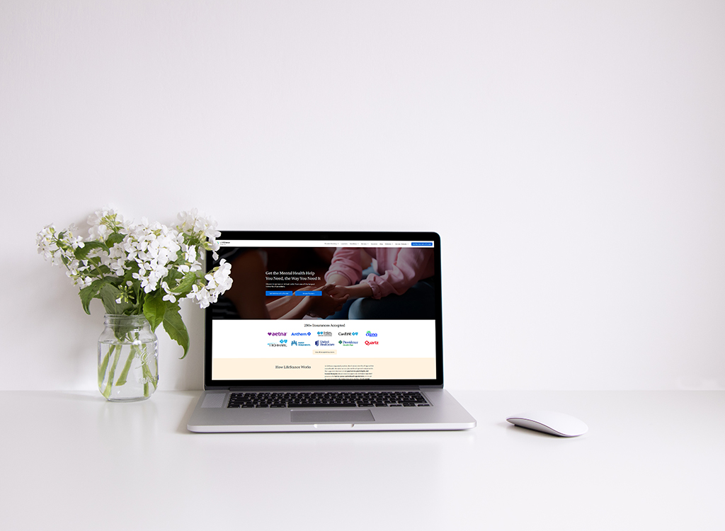 A modern workspace featuring a laptop displaying a mental health service website, next to a vase of fresh flowers and a sleek computer mouse, emphasizing a calm and inviting atmosphere for remote work.