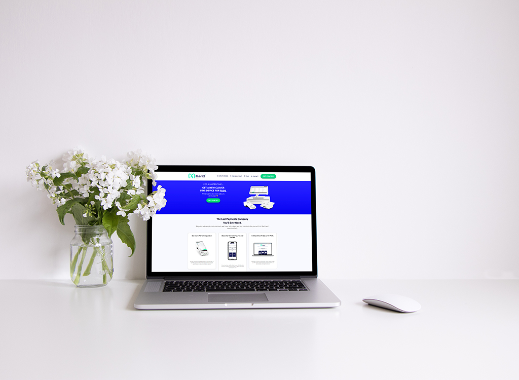 Laptop displaying a payment processing website on a clean desk, accompanied by a vase of white flowers and a wireless mouse, highlighting a modern workspace aesthetic.