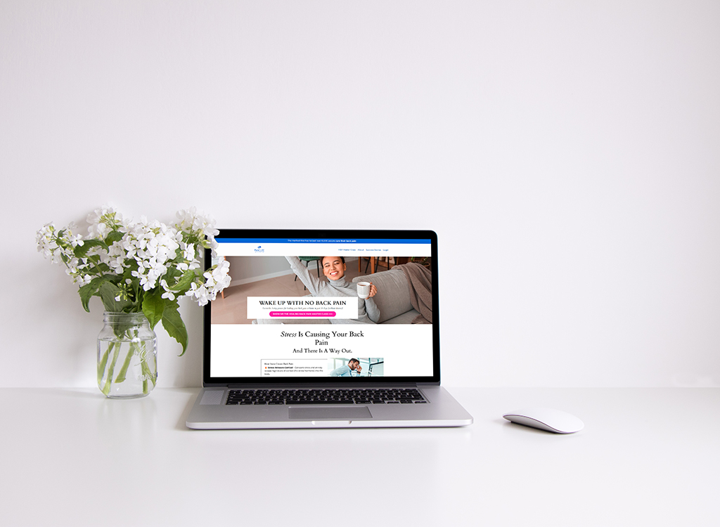 Laptop displaying a website focused on back pain relief, accompanied by a vase of white flowers on a clean desk. The webpage features tips for waking up without back pain, emphasizing stress as a contributing factor.