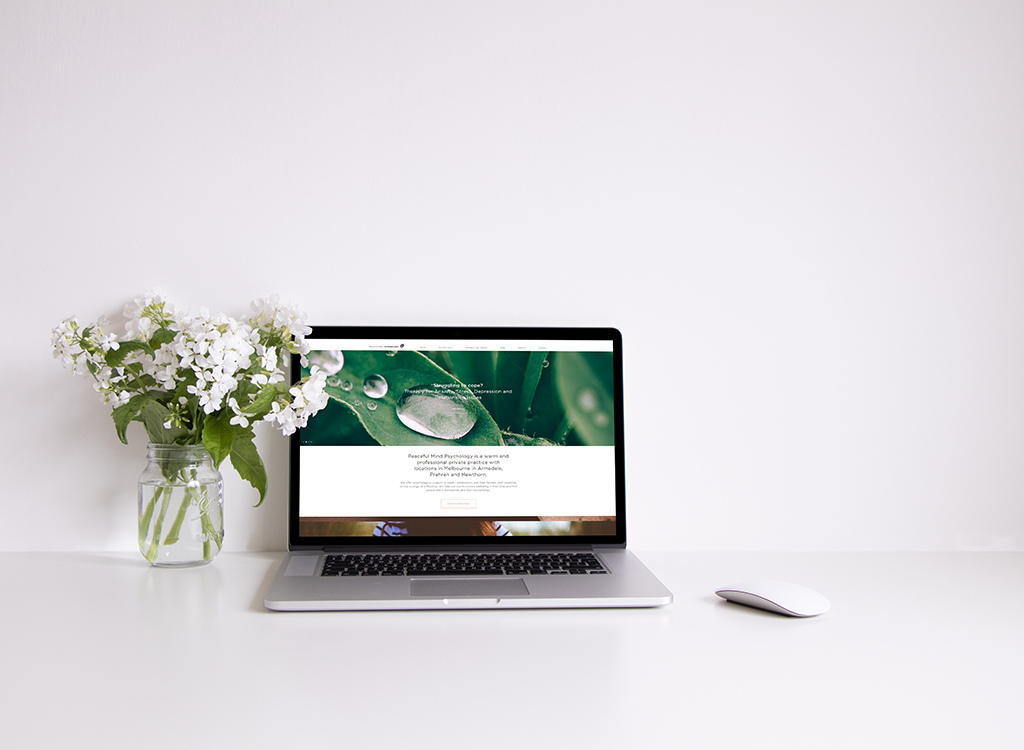 A modern laptop displaying a serene website on psychology sits on a clean white desk next to a vase of fresh white flowers, symbolizing tranquility and mental wellness.