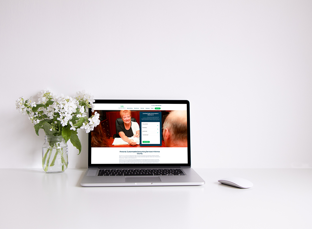 Laptop displaying a customizable accounting services website on a clean white desk with a vase of white flowers, emphasizing a professional and inviting workspace atmosphere.