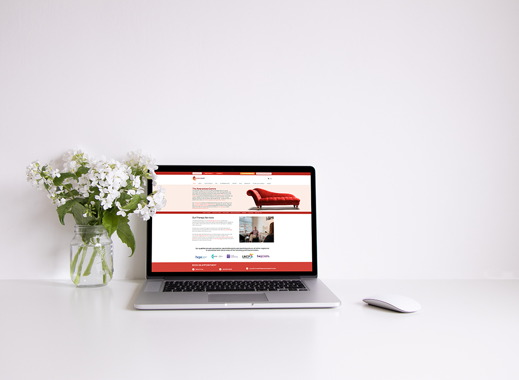 A modern laptop displaying a therapy website on a clean, minimalist desk with a vase of white flowers, emphasizing a calming and professional environment for mental health services.