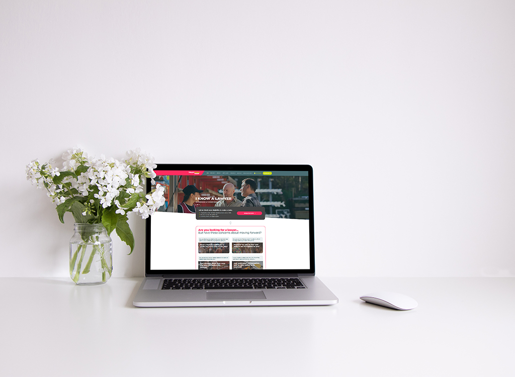 A modern laptop displaying a legal services website titled "I Know a Lawyer," positioned on a clean desk next to a vase of white flowers and a wireless mouse, ideal for online legal consultations.