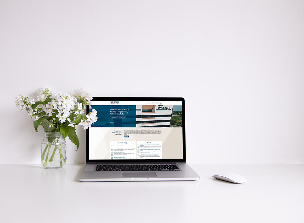 Laptop displaying a website for Wilentz, featuring legal services information, placed on a clean desk next to a vase of white flowers.